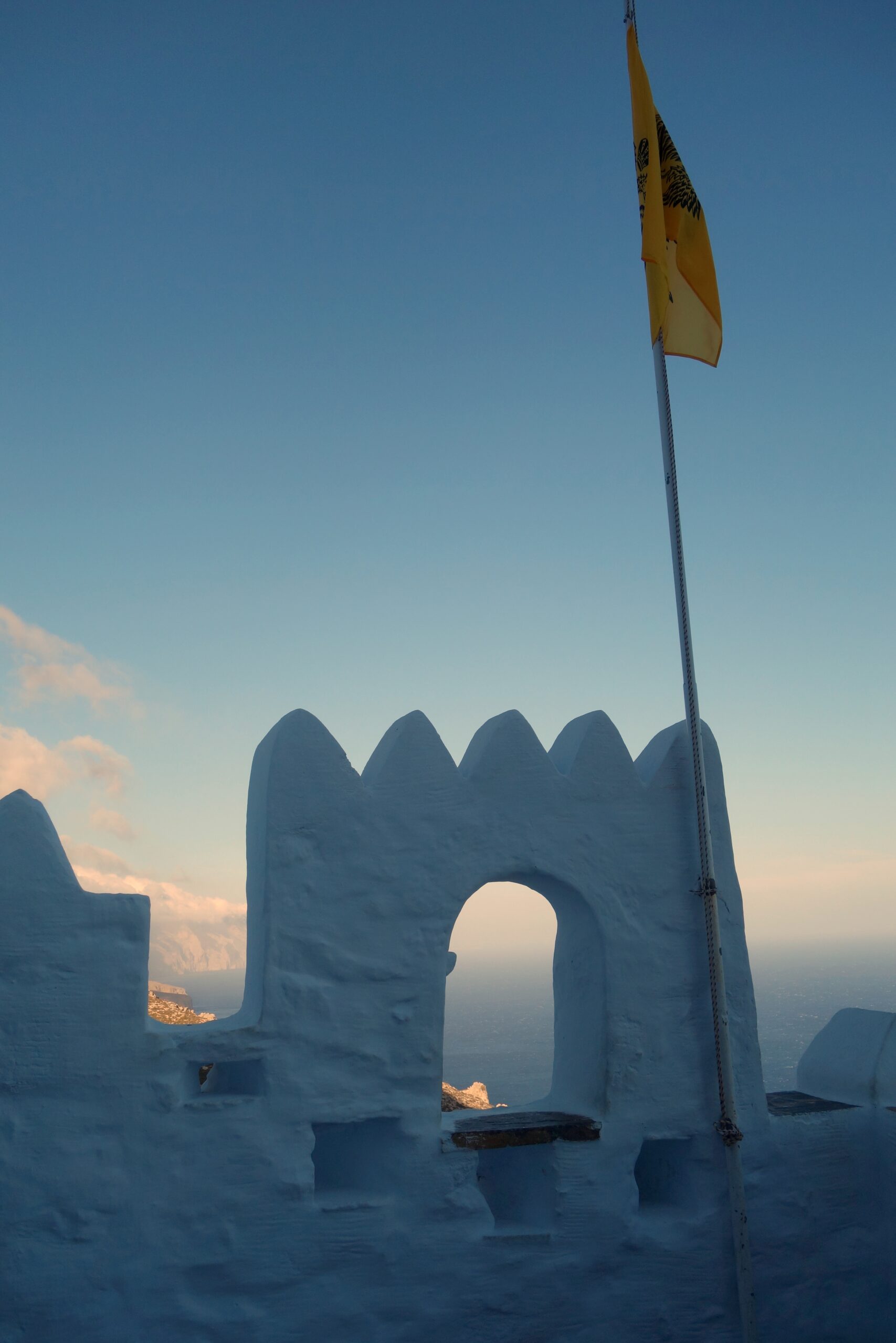 Ancient white monastery built into a towering cliff overlooking turquoise sea