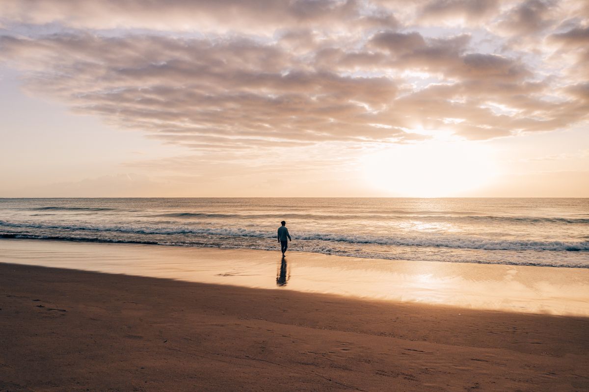 Lone traveler walking on an empty golden beach at sunset