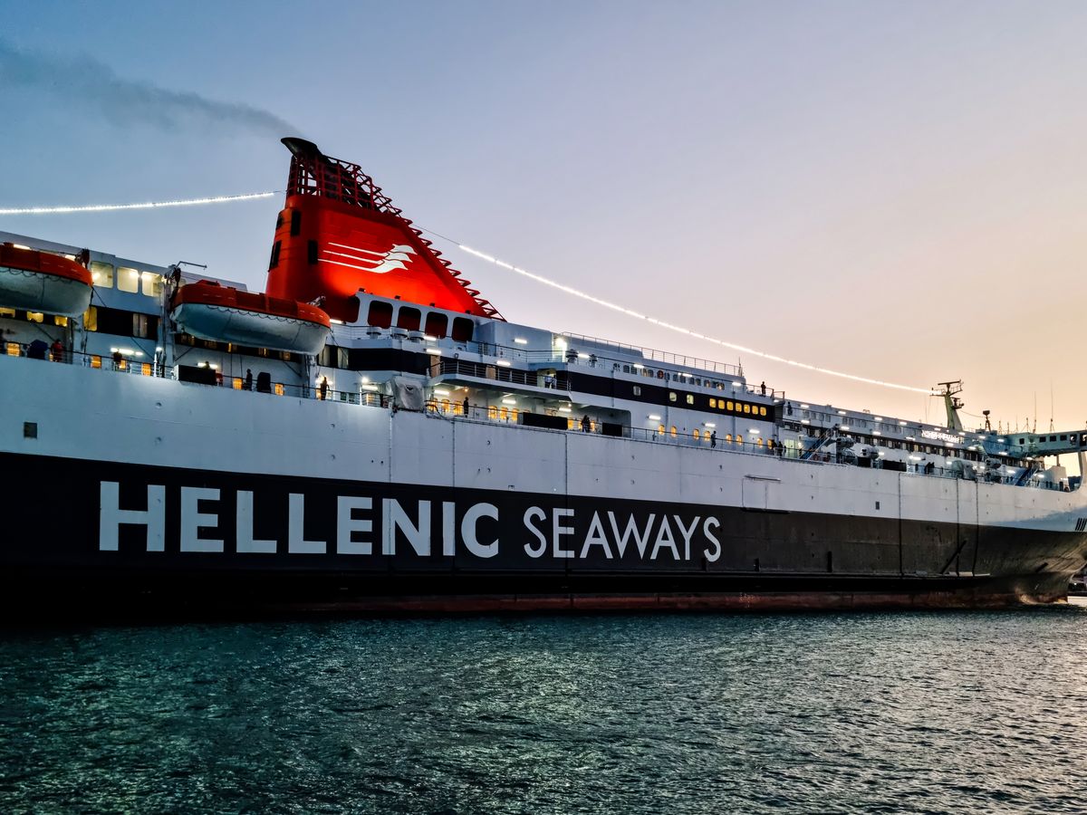 A Greek ferry sailing at sunset with orange sky and calm sea