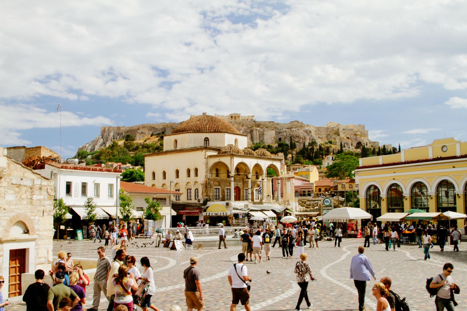 Monastiraki Square in Athens filled with people on a sunny afternoon with the Acropolis and Parthenon visible on the hill above
