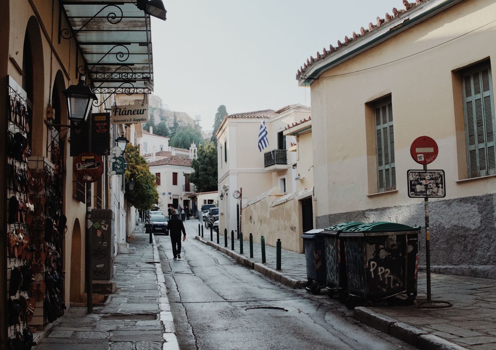 A quiet street in the Plaka neighbourhood of Athens with traditional shops and a Greek flag hanging from a balcony