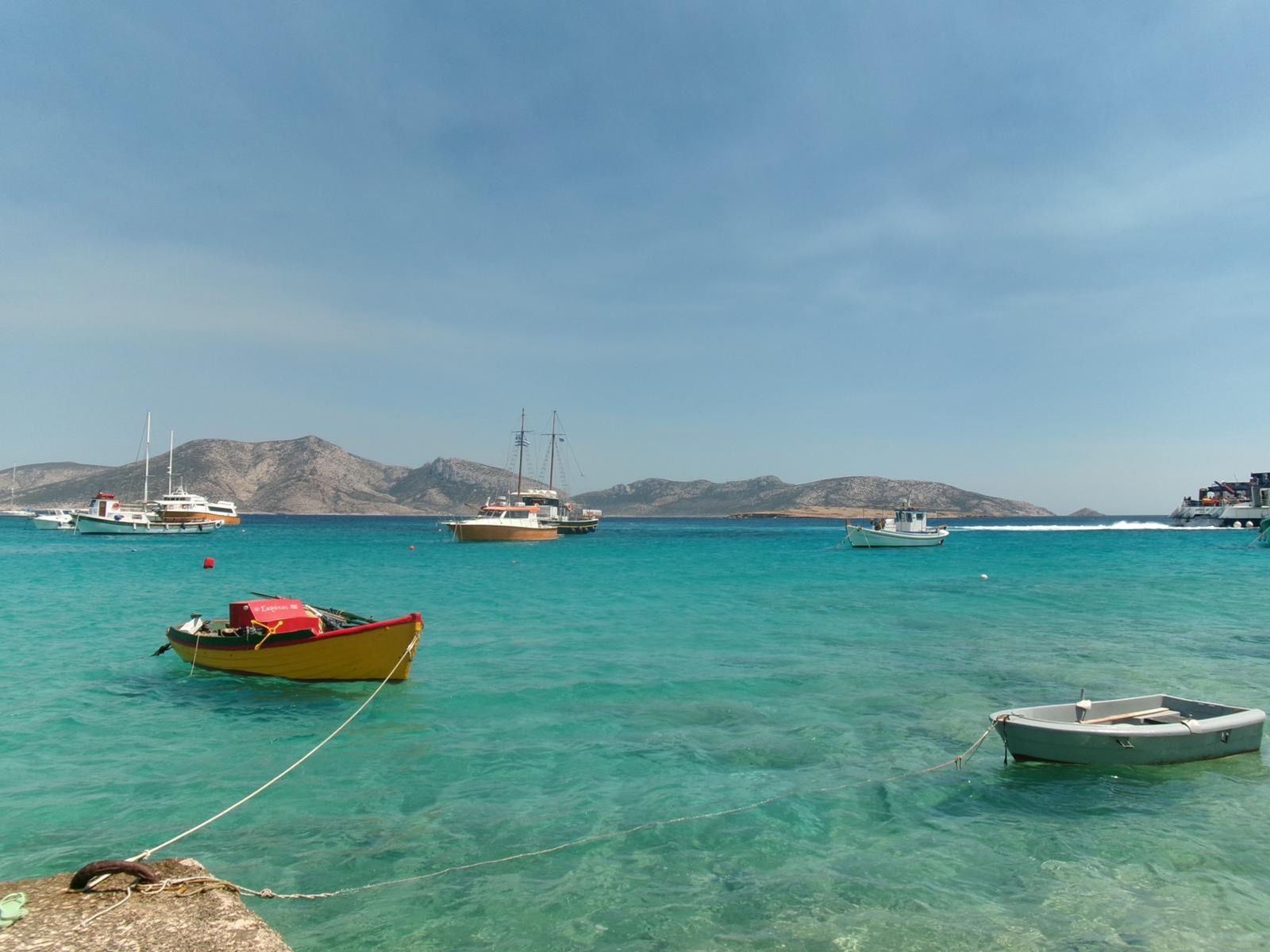 Small boats on the clear turquoise waters near the coast of Milos, Cyclades, Greece