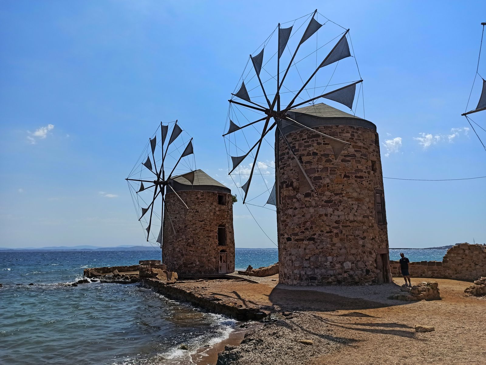 Historic stone windmills along the Chios coastline under a clear blue sky