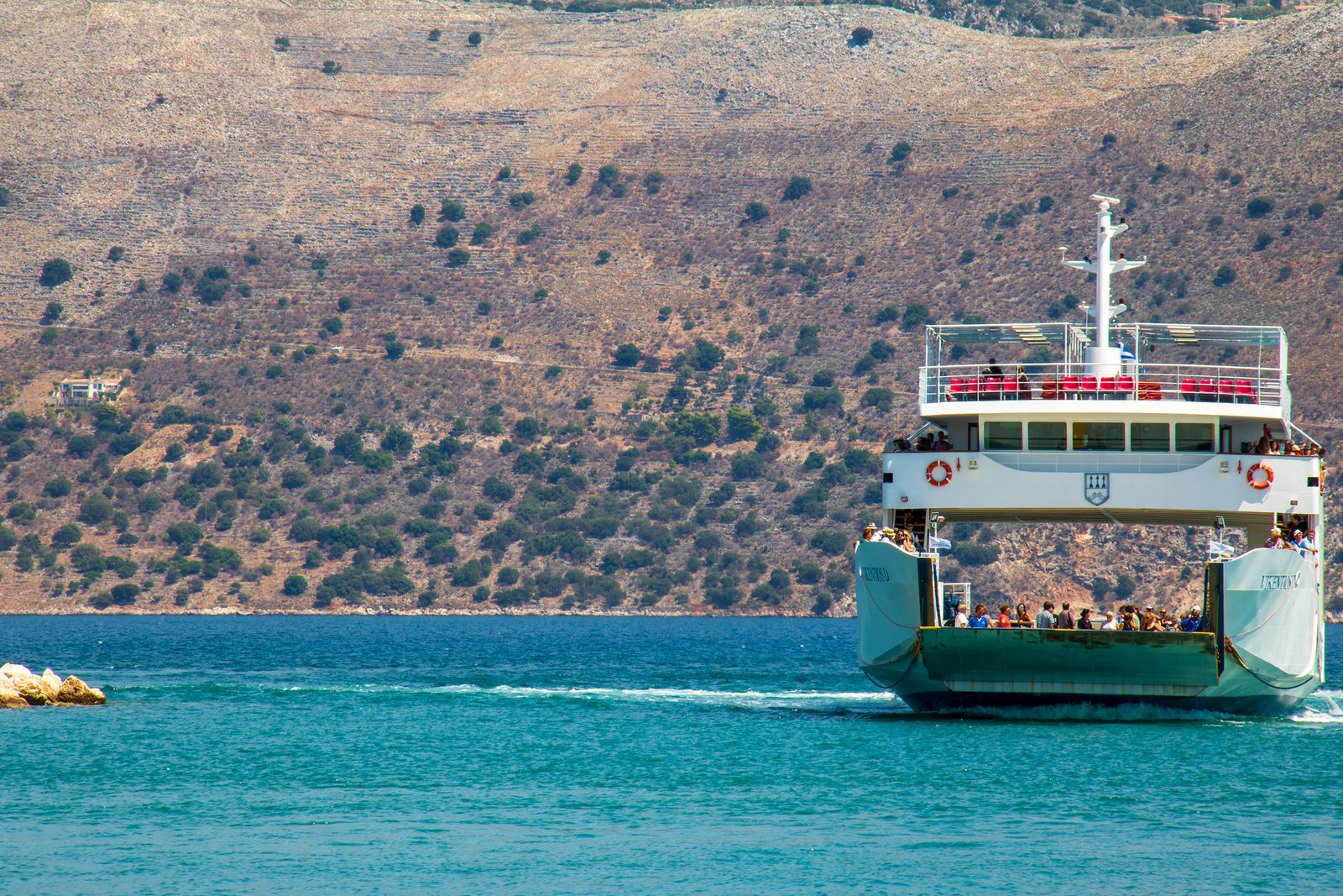 Passenger ferry crossing the clear blue Ionian Sea with rugged Greek coastline in the background