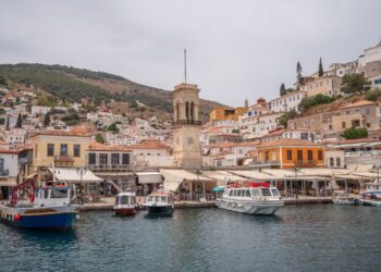 Hydra harbour with the historic clock tower of the Church of the Assumption rising above stone houses and moored boats