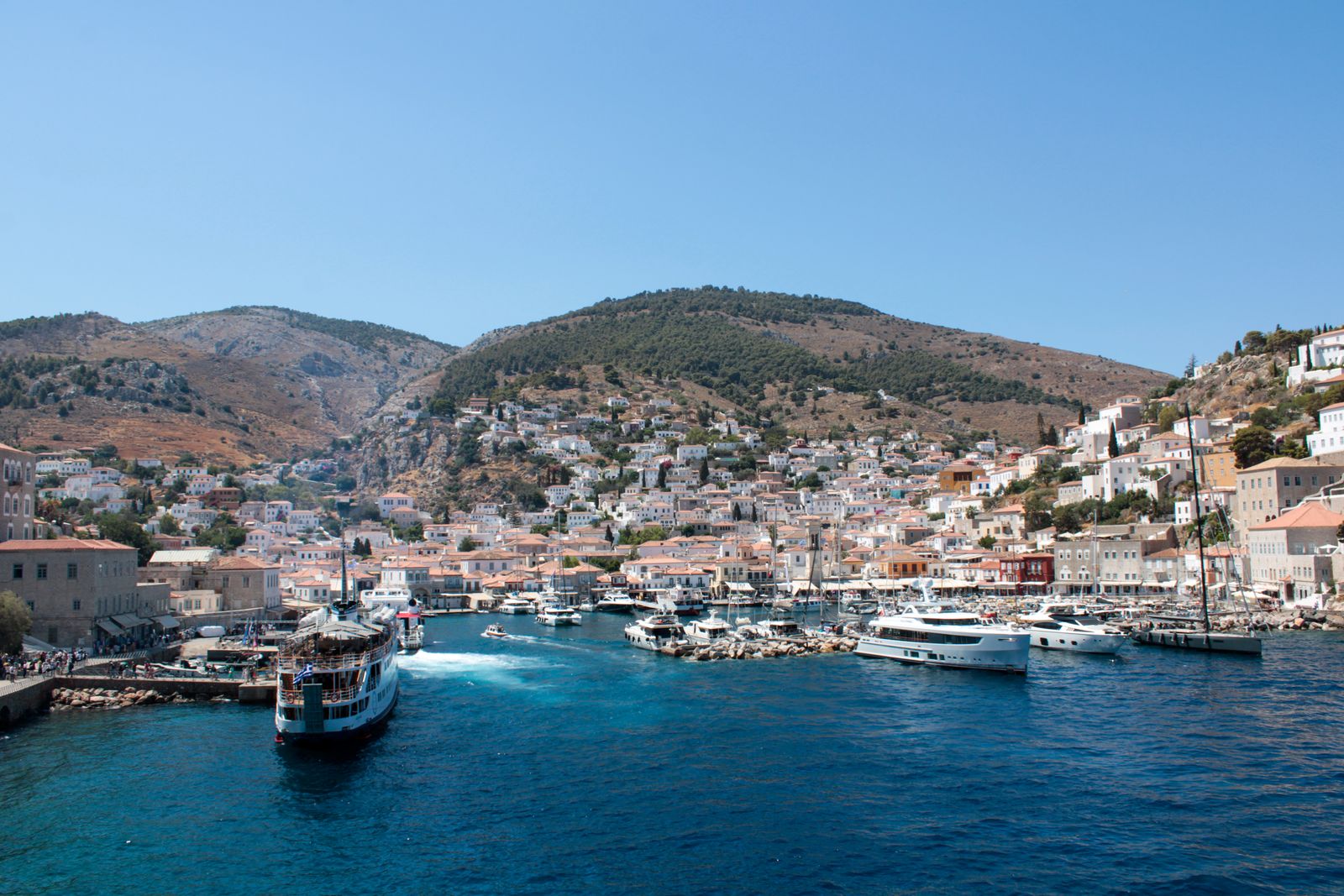Panoramic view of Hydra Island harbour with traditional stone buildings climbing the hillside above the waterfront