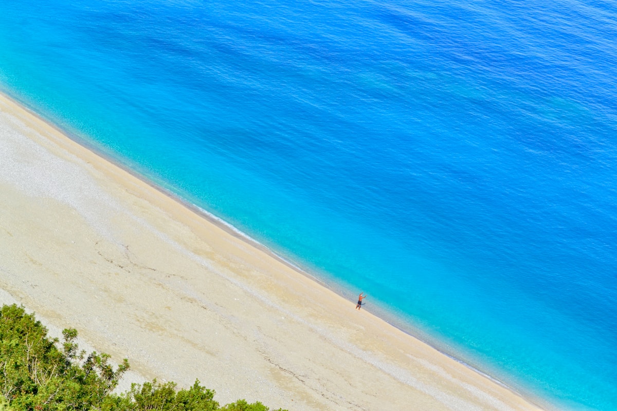 Aerial view of Myrtos Beach showing the dramatic white pebble crescent and intense turquoise water between two limestone cliffs, Kefalonia