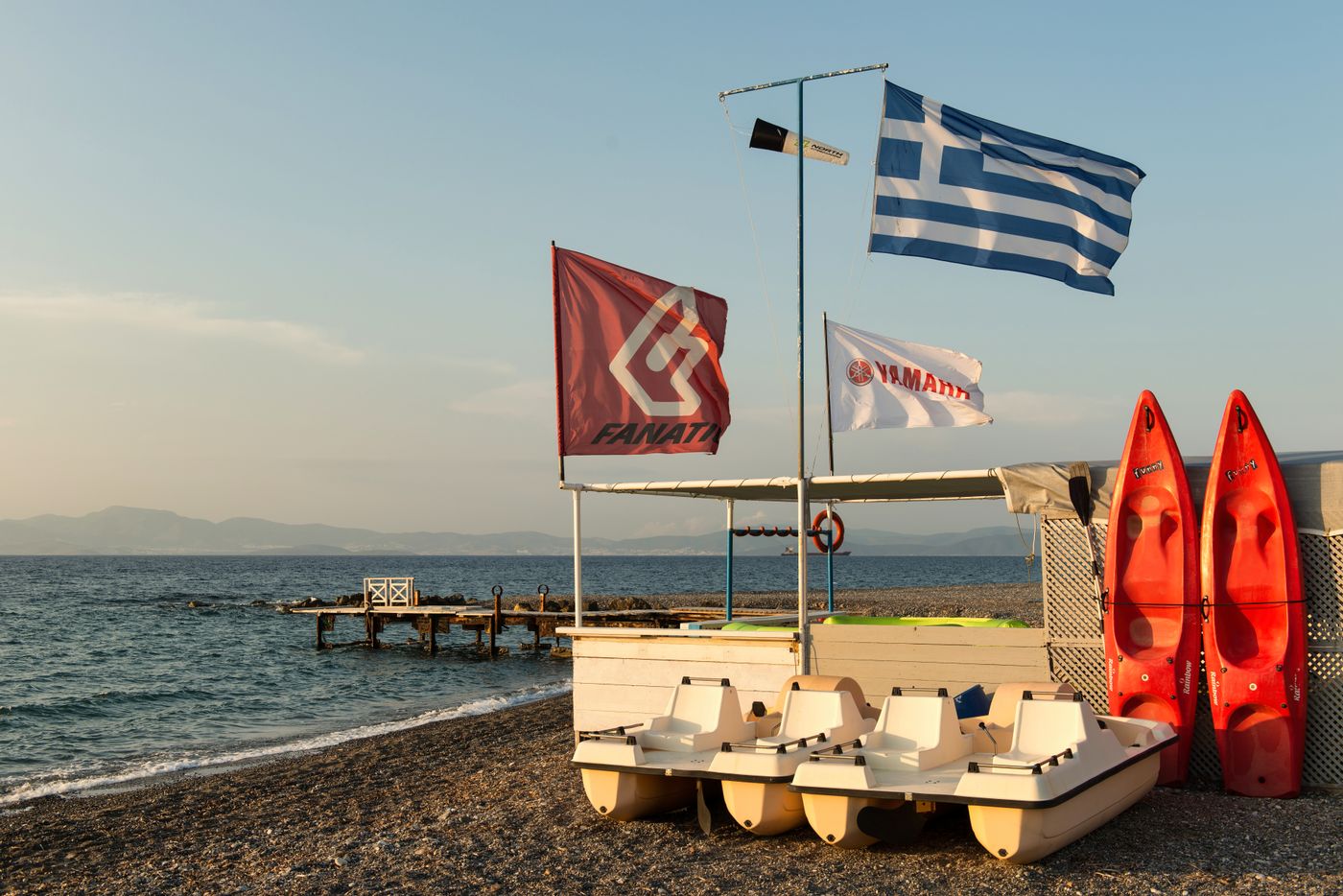 Shallow sandy beach on Kos island with paddle boats and Greek flags under a summer sky