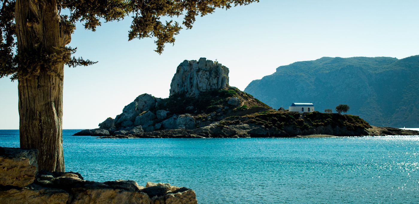 Rocky islet rising from clear blue waters off the coast of Kos island Greece