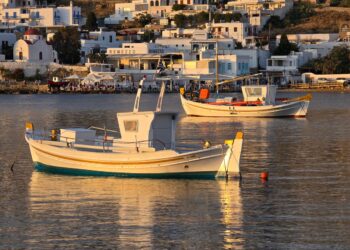 Colourful fishing boats moored in a Greek island harbour at sunset with traditional harbourside buildings