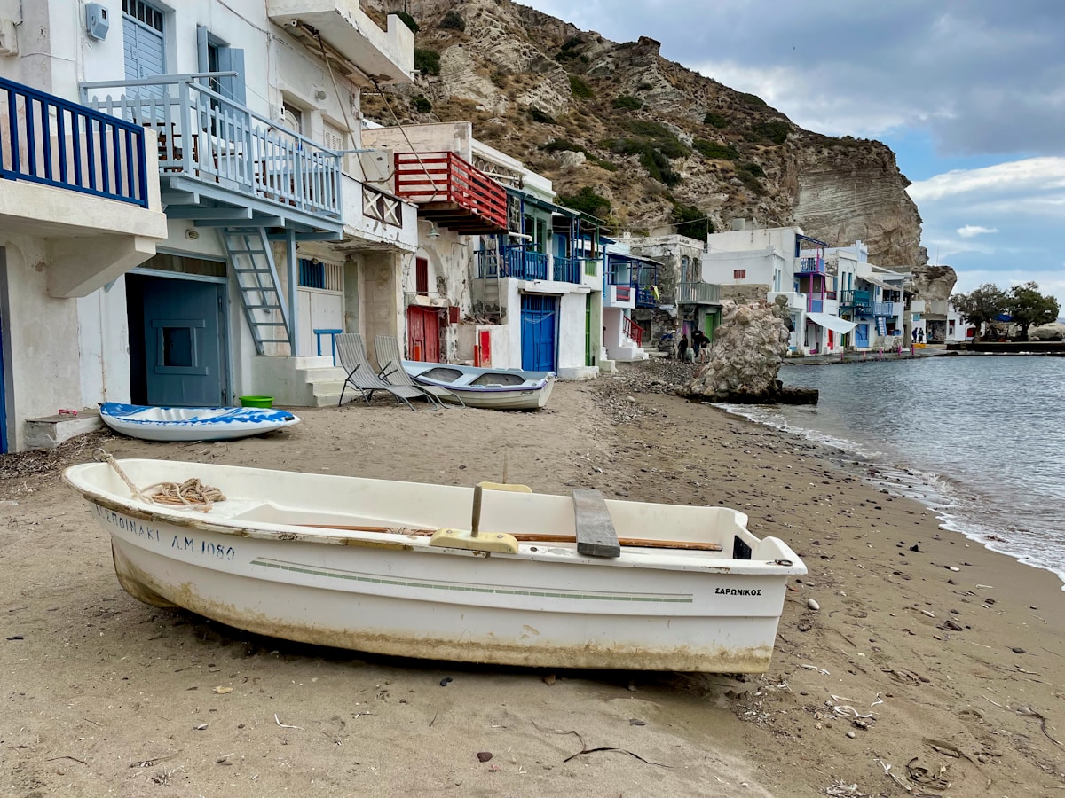 Colourful syrmata boathouses and a wooden fishing boat on the waterfront at Klima village in Milos, Greece