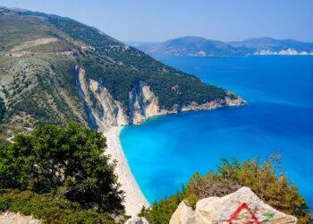 Aerial view of Myrtos Beach with turquoise waters and white pebble shore surrounded by limestone cliffs in Kefalonia, Greece