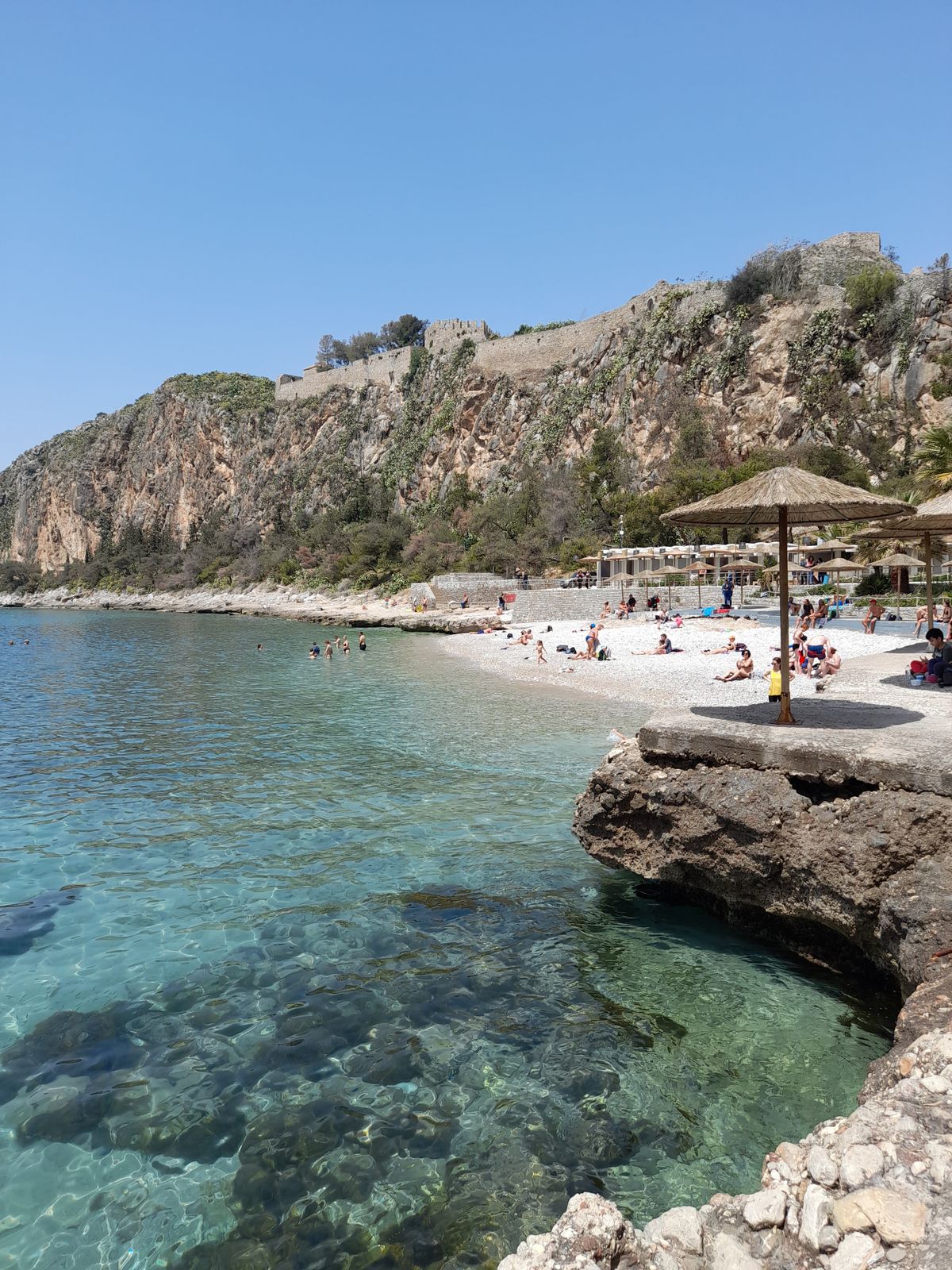 Clear turquoise waters at Arvanitia Beach beneath the fortress walls of Nafplio