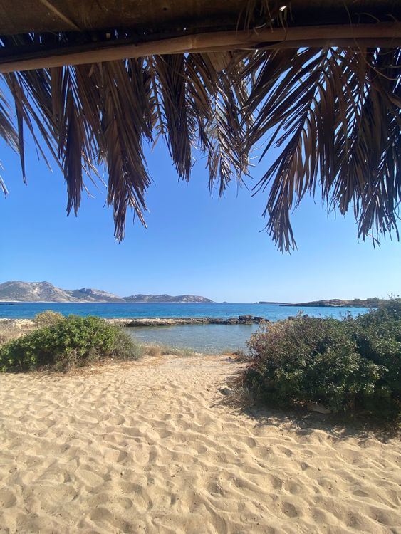 Sandy beach with clear blue water and distant green hills in Naxos, Greece