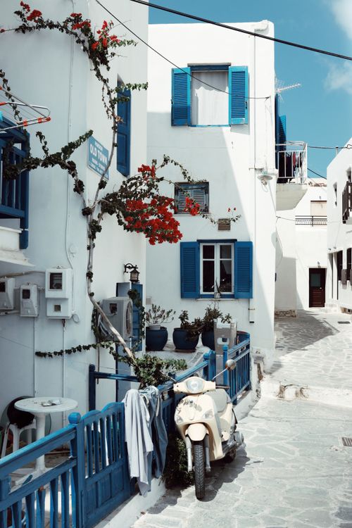 Charming blue and white alley in Naxos with bougainvillea and a parked Vespa