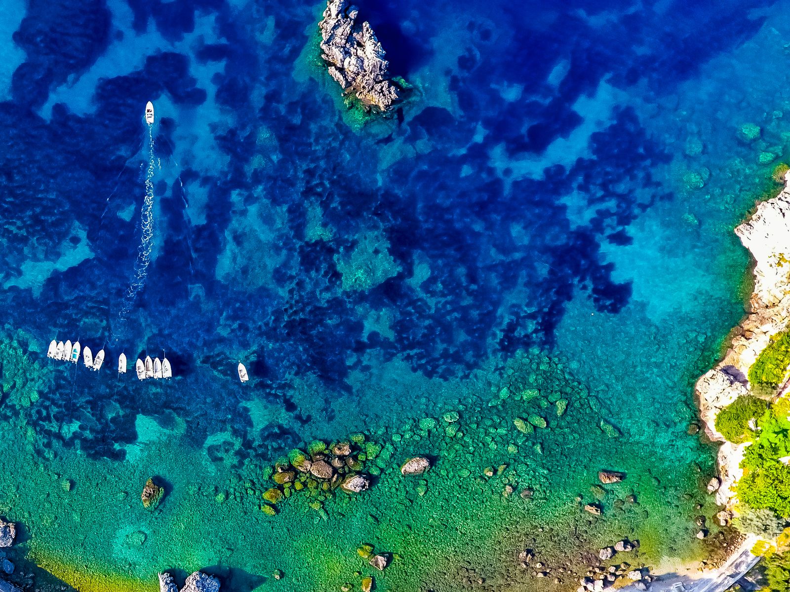 Aerial view of the turquoise bays of Paleokastritsa with boats anchored in clear water along Corfu's western coast