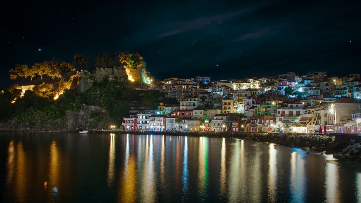 Parga harbour illuminated at night with colourful reflections on calm water