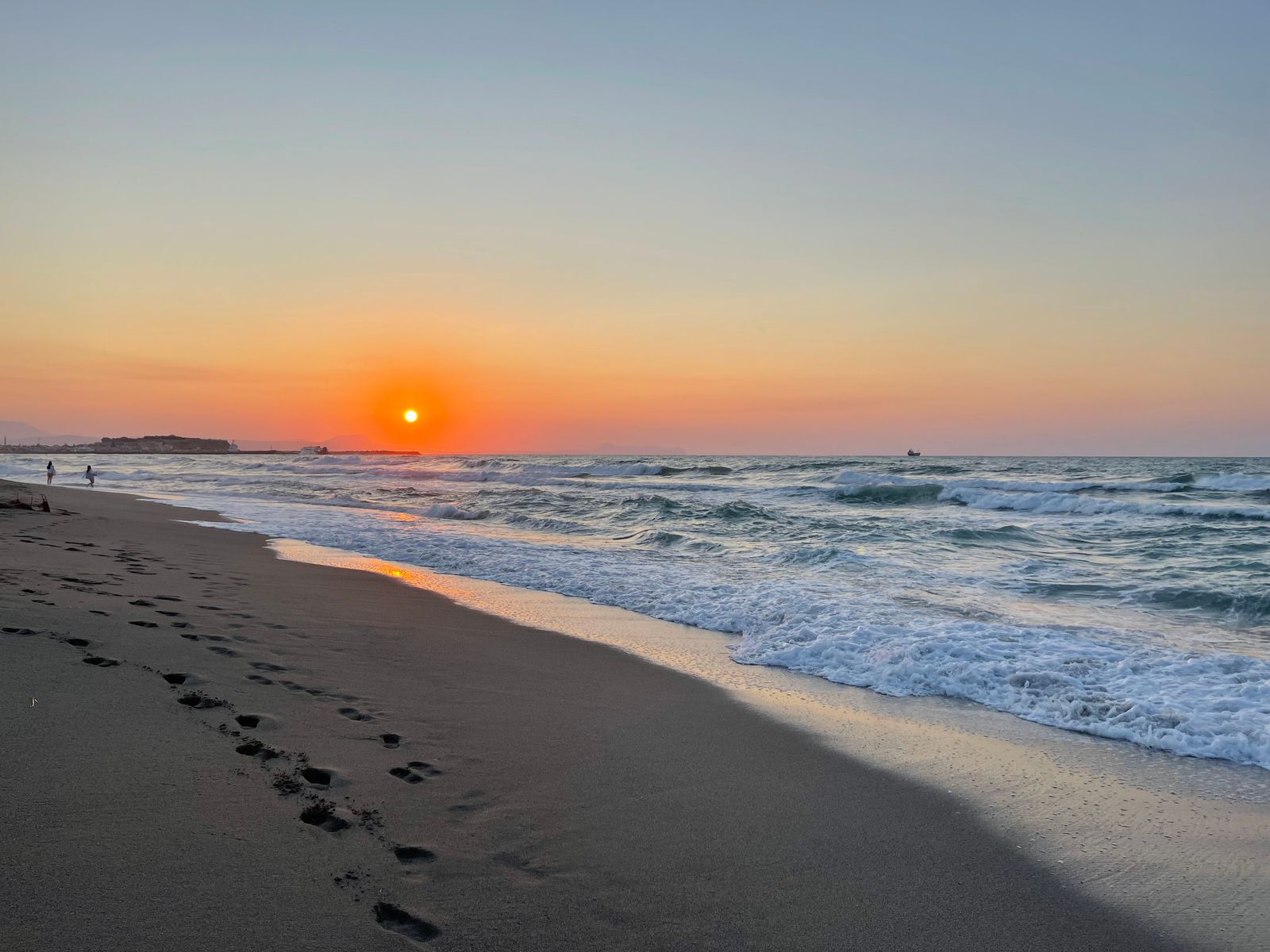 Sunset over Rethymno Beach with footprints in the sand and gentle Mediterranean waves