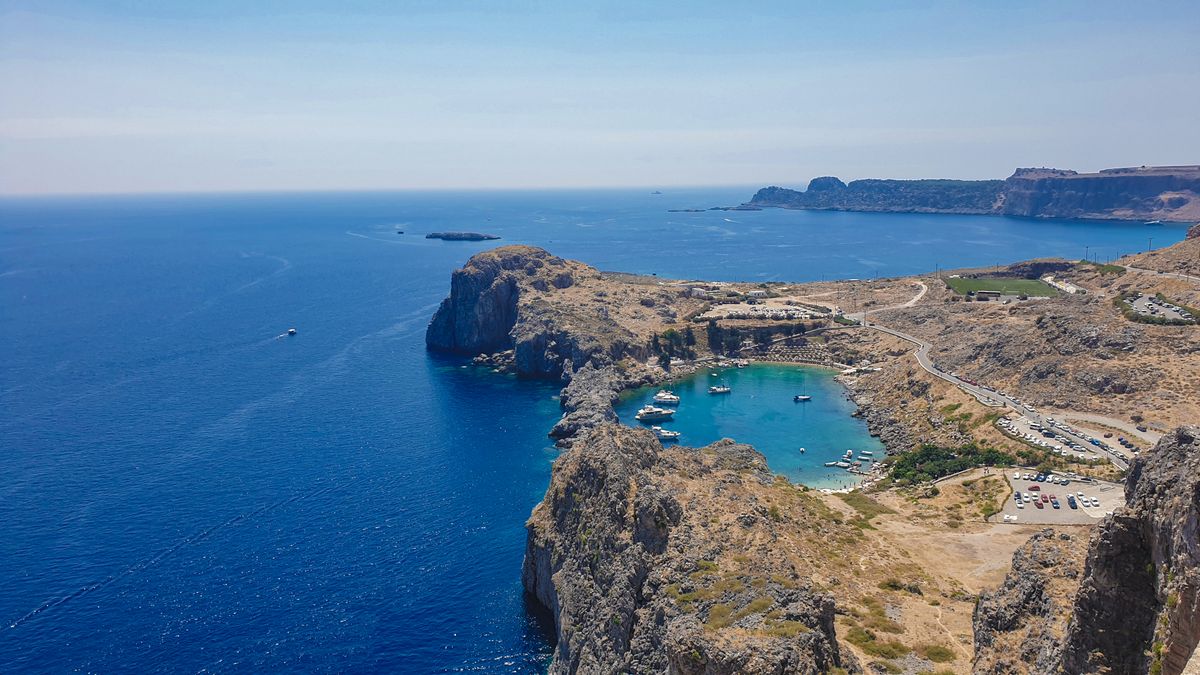 Aerial view of St Paul's Bay in Lindos, Rhodes, showing turquoise water enclosed by rocky cliffs