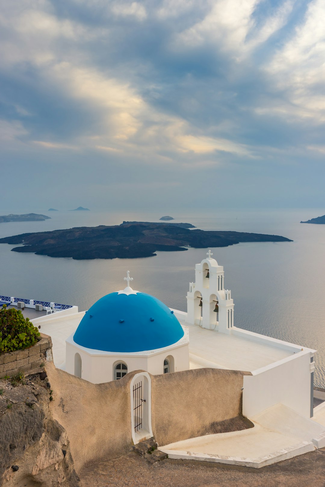 Blue-domed church and bell tower overlooking the volcanic islands in the Santorini caldera