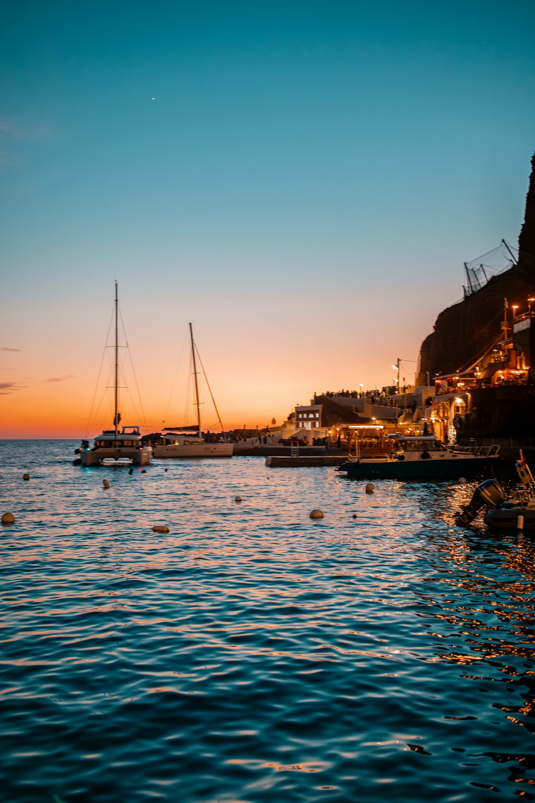 Fira harbour illuminated at sunset with boats anchored below the caldera cliffs in Santorini