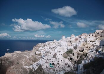 Panoramic view of whitewashed buildings and blue domes along the caldera rim in Oia, Santorini