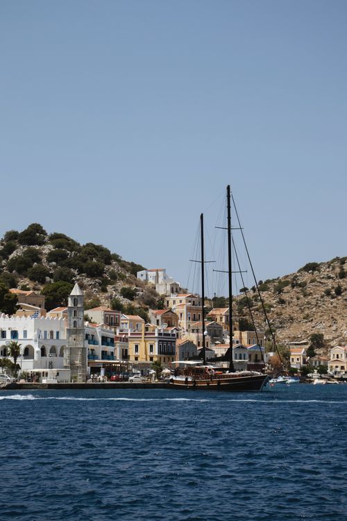 Symi harbour with colourful neoclassical houses and a sailboat moored in calm waters, Greece