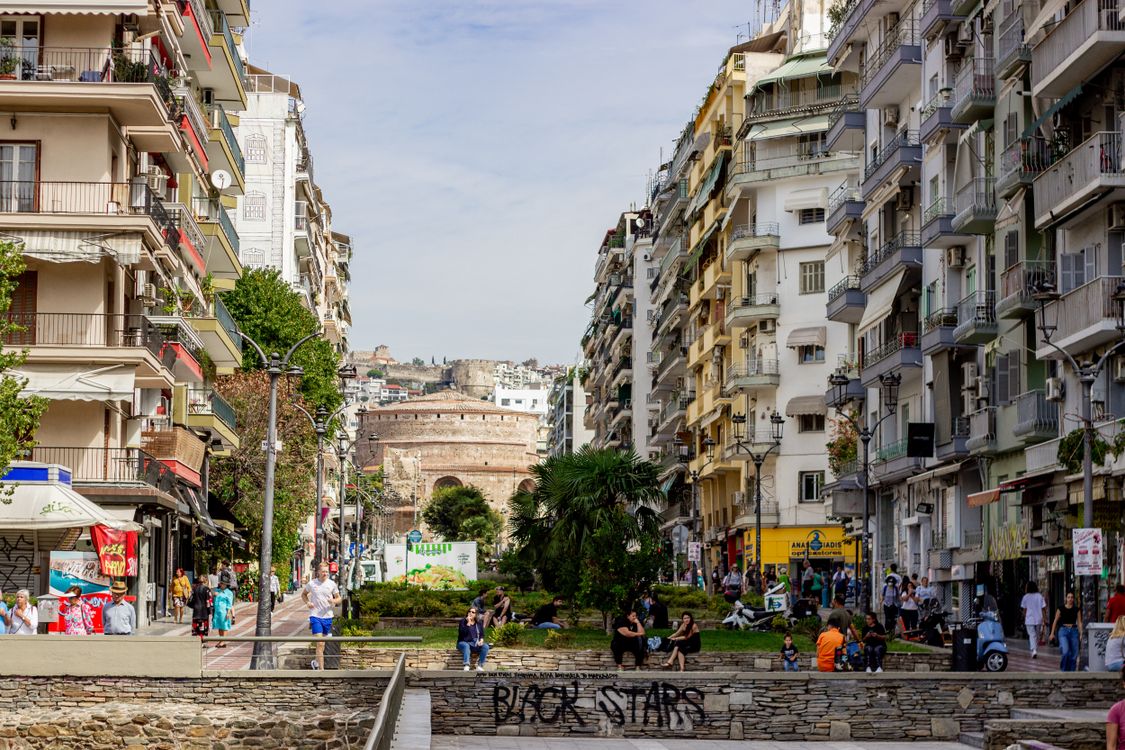 A busy street in central Thessaloniki with the Rotunda of Galerius visible in the background among modern buildings and parked cars