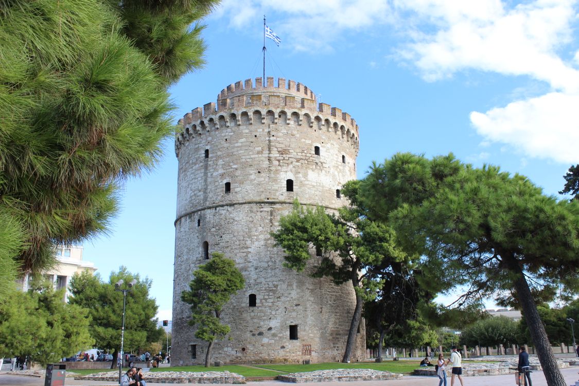 The White Tower of Thessaloniki surrounded by green palm gardens under a clear blue sky
