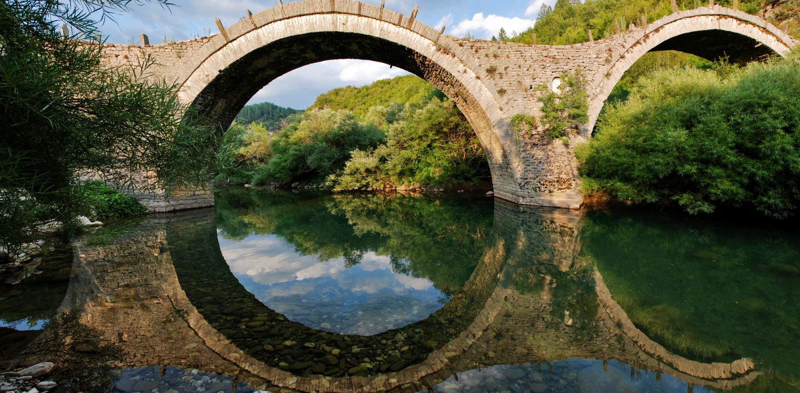 The stone arch bridge at Kipoi reflected in the calm waters of the Voidomatis river basin