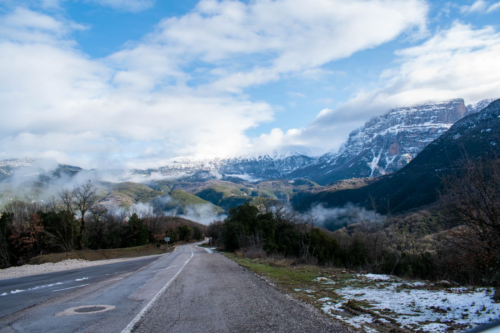 A mountain road winding through the Zagori landscape near Monodendri with snow-dusted peaks beyond