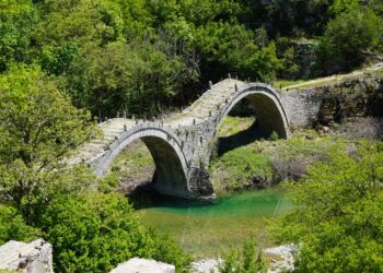 The three-arched Plakidas stone bridge spanning a stream in Zagori, surrounded by forest