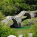 The three-arched Plakidas stone bridge spanning a stream in Zagori, surrounded by forest