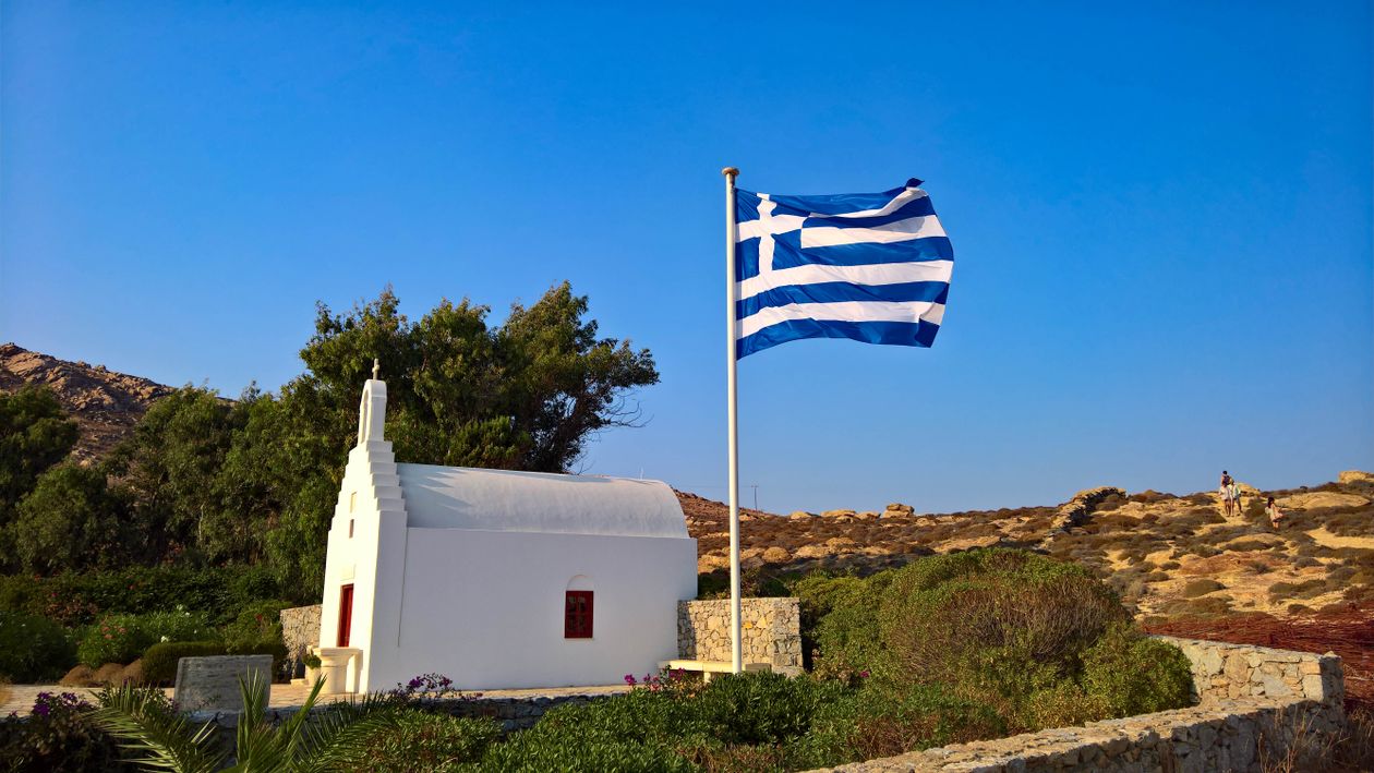 White church with Greek flag on a hilltop in Ios island, Cyclades