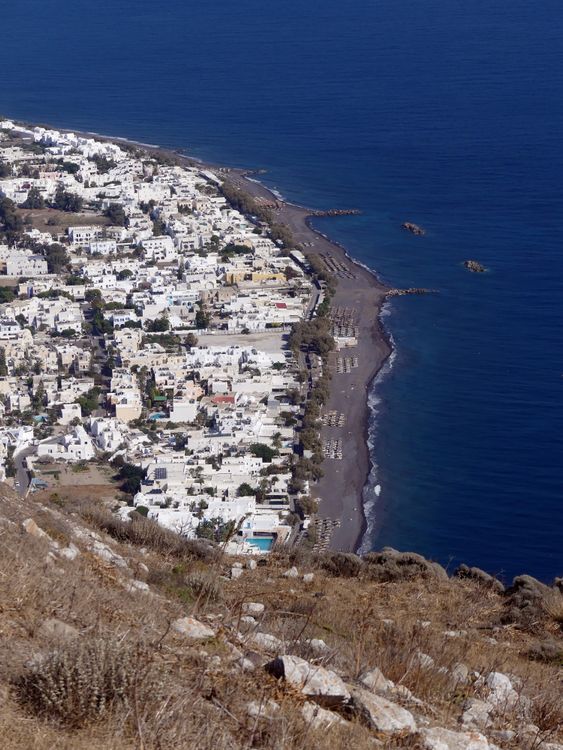 Aerial view of Kamari beach and town on Santorini's eastern coast with dark volcanic sand